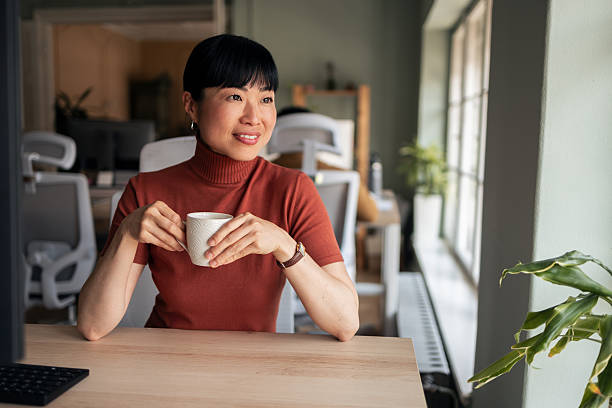 istock Woman Relaxing in Office, Holding Coffee Cup by Window 2251521800