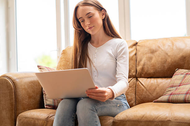 istock Young woman sitting on couch while using laptop in bright room during daytime hours 2251522528