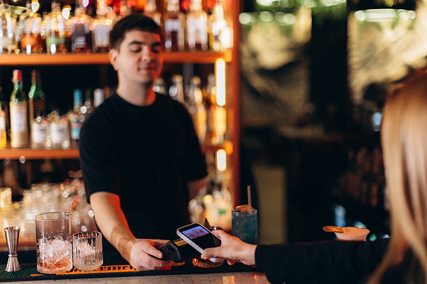 istock Customer Makes Contactless Payment to Bartender in Trendy Bar Setting 2251533175