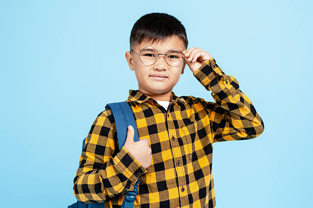 Elementary school boy in plaid shirt and glasses, smiling against blue background