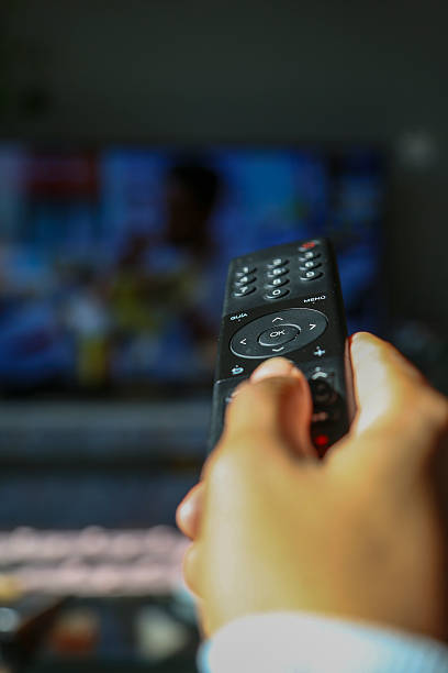 istock Light-skinned African American woman's hand holding a remote control pointing at the television 2251538401