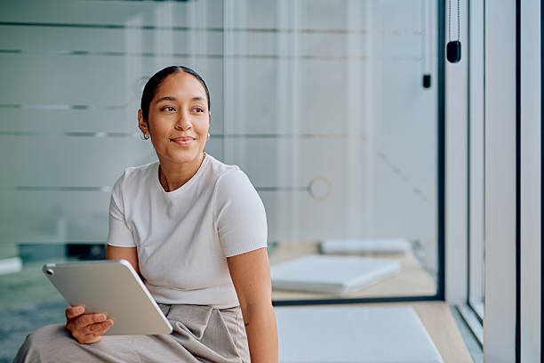 istock Woman holding tablet looking thoughtfully out window 2251539234