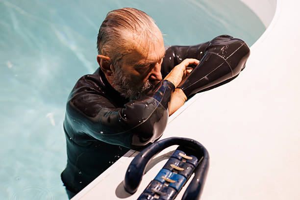 istock Grey haired diver in wetsuit resting near neck weight at poolside 2251544609
