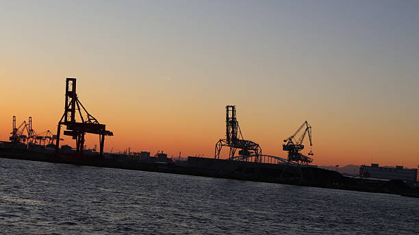 istock An expansive harbor at sunset, with the sky transitioning from light to dark as it stretches over the ocean. On the horizon, a few cranes are visible, indicating port activity 2251546080
