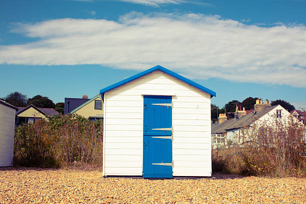 A white hut with a blue roof sits on the Kingsdown beach in Dale. It is a sunny afternoon with a blue sky and yellow pebbles.