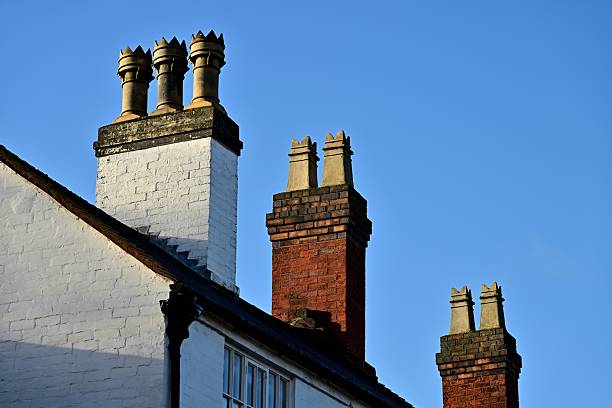Three mixed-brick chimneys with decorative pots, clear blue sky, architectural detail highlights.