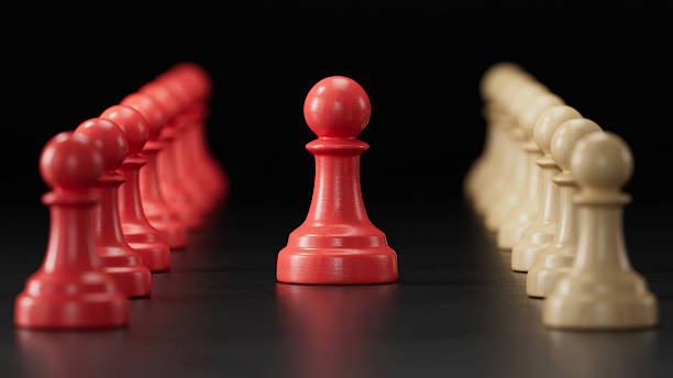 istock Single Red Pawn Amid Two Pawn Groups: Embodying Individuality on black Background 2251548198