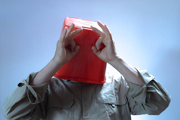 Man with red plastic bucket over his head mimicking eyes with his hands