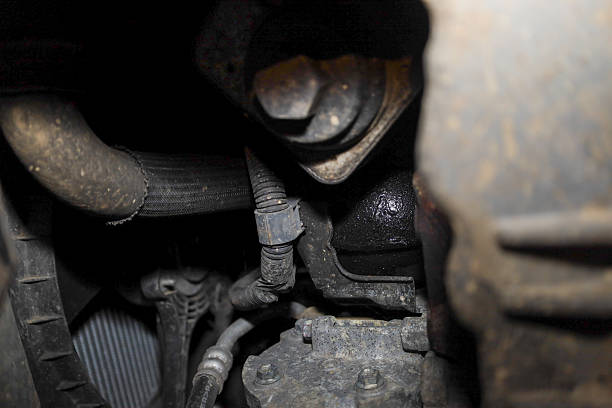 istock ​A deep view into a dirty, oily car engine bay, showcasing components like a hose, electrical harness, a large bolt, and an apparatus with a noticeable oil leak. 2251550073