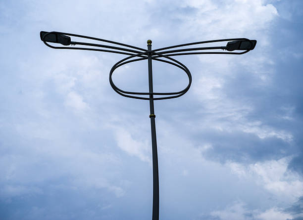 Modern street light with a tall pole and curved bracket holding dual LED lamp heads, photographed against an overcast, cloudy sky.