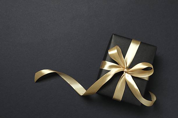istock Beautiful gift box with a golden bow on black background 2251552305