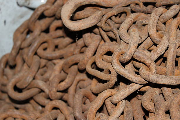 Many rusty metal chains are stacked in a storage area. The chains are tangled and uneven, with some dirt and dust covering the surface. The scene appears to be well lit.