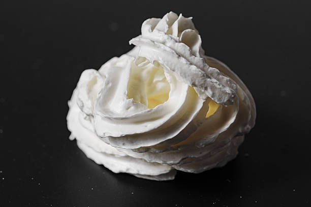 Whipped milk cream from the tube is squeezed onto a black surface. A delicious milk dessert.