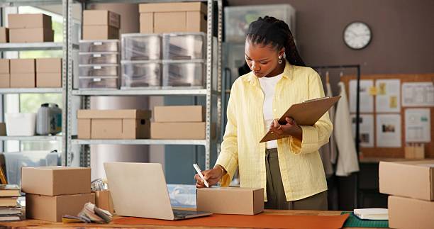 istock Black woman, writing and clipboard for logistics at startup with notes, supply chain and inventory management. Mature person, label and box for e commerce, fashion or checklist for order distribution 2251565593