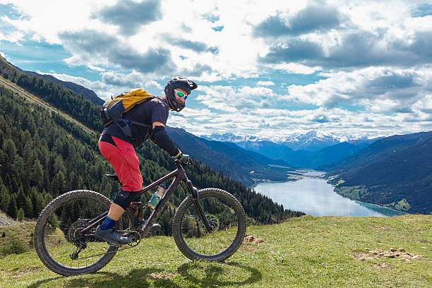 An experienced and well equipped male mountain biker is riding at a very scenic lookout with Lake Reschen in the background. It is an artificial lake in the western portion of South Tyrol, Italy, approximately 2 km (1 mi) south of the Reschen Pass, which forms the border with Austria, and 3 km (2 mi) east of the mountain ridge forming the border with Switzerland. The area is famous for mountain biking, cycling, hiking and skiing.Canon EOS 5D Mark IV, 1/800, f/8, 28 mm.