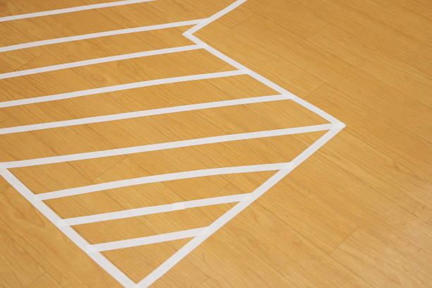 White tape on a wooden floor forms a trapezoid with parallel lines, creating a three-dimensional optical illusion.
