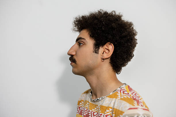 Profile view of pensive young man against white background.  Man with mustache and curly hair wearing vibrant t-shirt.