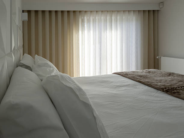 istock A bright modern bedroom with a features a neatly made double bed with white linens, textured blanket and warm wood floor, as soft daylight filters through long beige curtains for a peaceful stay. 2251571534