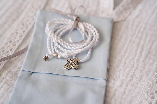 A delicate necklace with a silver cross pendant rests on light blue fabric. The braided cord adds elegance to this thoughtful piece, perfect for special occasions.