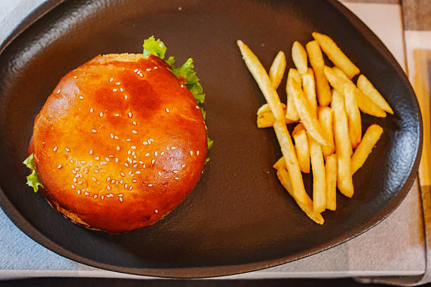 A freshly made burger with a golden sesame bun, lettuce, and served alongside crispy golden fries on a black plate. Perfect for a tasty meal.