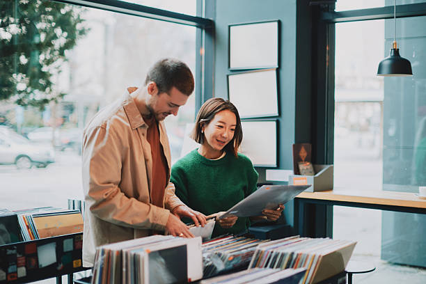 A cheerful adult couple browses vinyl records in a bright store. Casual clothing and warm daylight create a cozy, musical moment of shared discovery.