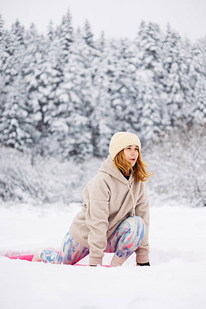 The young woman balancing in Low Lunge Yoga Pose during her exercise outdoor in snow winter day