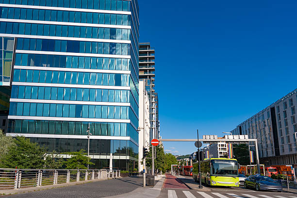 Oslo traffic and pedestrians on Dronning Eufemias gate in Norway with modern glass barcode buildings and blue sky.