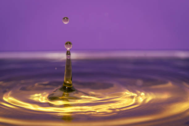 High speed macro of golden water column and droplets against purple background, colorful abstract concept of motion and energy.
