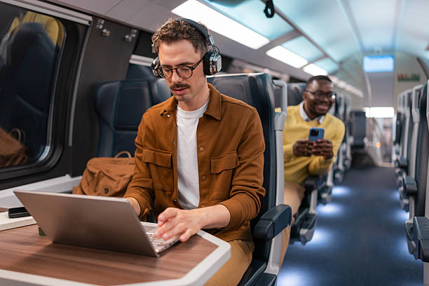 istock Young man is using a laptop while traveling on a modern train with other passengers 2251587672