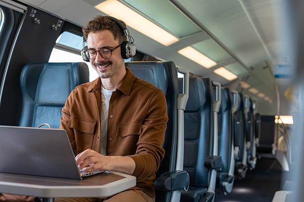 istock Young man with headphones working on a laptop inside a modern train 2251587906