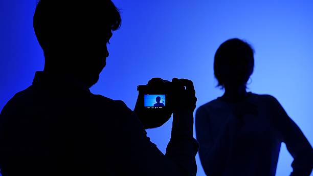 Backstage at a professional studio with a silhouette of a photographer capturing a model with a camera against a blue lit background.
