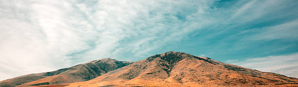 A mountain range with a clear blue sky in the background. The sky is dotted with clouds, giving the scene a peaceful and serene atmosphere