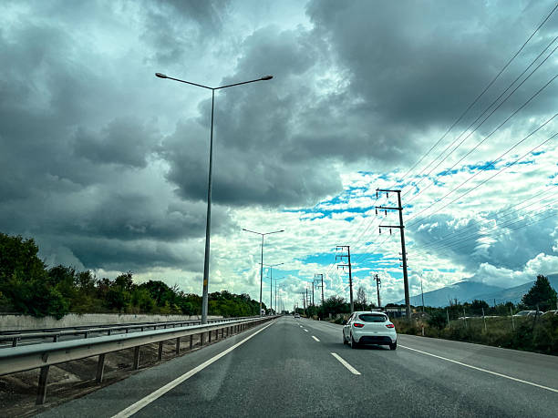Car Driving on Asphalt Road Under Dramatic Cloudy Sky with Power Lines