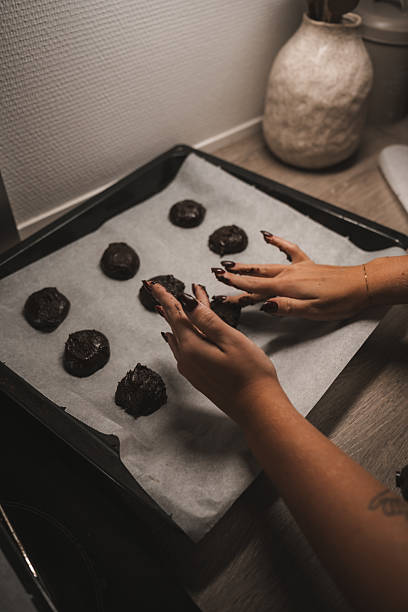 istock Hands shape chocolate cookie dough on a baking tray lined with parchment paper in a warm kitchen. The soft lighting creates a comforting atmosphere, perfect for baking 2251609078