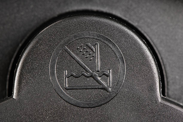Extremely close-up shot of an embossed warning symbol on textured black plastic, showing a crossed-out shower and water waves, indicating \