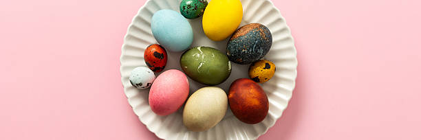 istock A collection of vibrant Easter eggs in various colors is artfully arranged on a white plate, set against a soft pink background, capturing the essence of the holiday's decorations, banner 2251615509