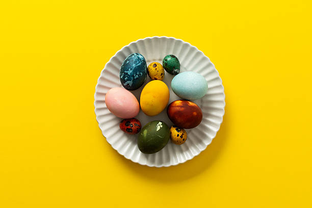 istock A variety of beautifully painted Easter eggs in different colors and patterns are placed on a delicate white plate. The vibrant hues stand out against the cheerful yellow backdrop 2251615520