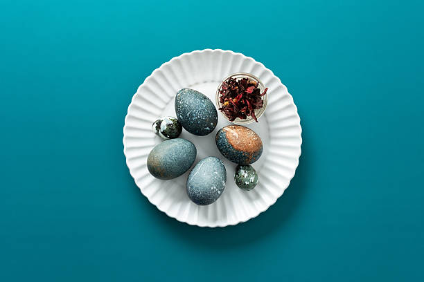 istock A decorative plate displays several uniquely colored Easter eggs, showcasing shades of blue and brown, a small bowl filled with dried flowers hibiscus, how to dye eggs dark marble blue 2251615531