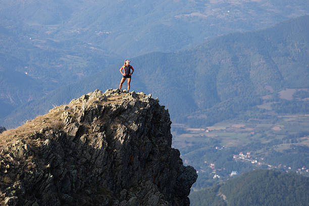 Woman is standing on a rock, she is taking a break from running in the mountains and enjoying the view.