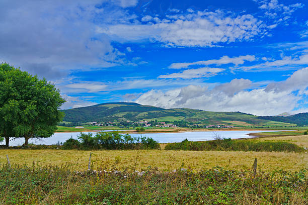 Ebro reservoir and surrounding landscape with a small rural village and hills under a vibrant blue sky dotted with clouds in Spain
