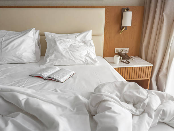istock Inviting hotel bed with soft white pillows, open book and morning coffee creating a peaceful atmosphere in a bright modern room with warm wooden accents and natural light 2251623925