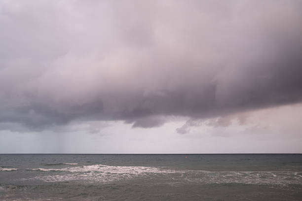 Heavy storm clouds are forming over a choppy sea, with visible streaks of falling rain creating a dramatic and moody atmosphere across the vast open water