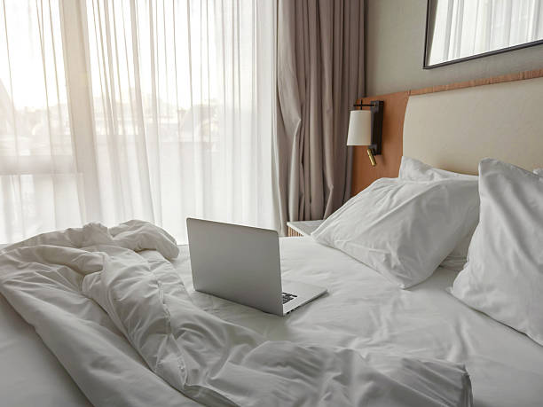 istock Bright hotel room with soft white bedding, pillows and an open laptop on an unmade bed, creating a cozy atmosphere for remote work, relaxation, travel comfort and modern lifestyle 2251628845