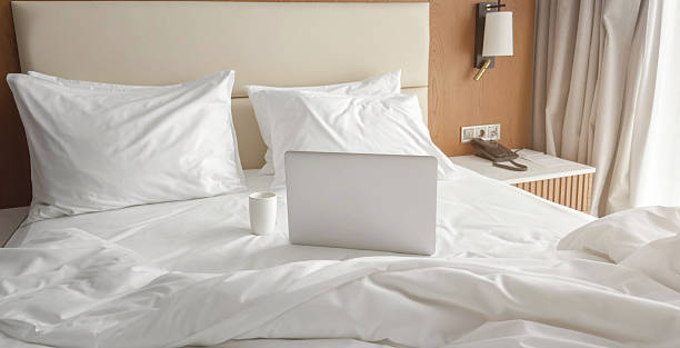 Cozy hotel room interior with soft white bedding, pillows, laptop coffee cup creating calm workspace atmosphere with natural light, comfort modern design perfect for travel, hospitality themes