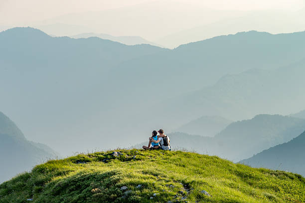 istock Two People Sitting on a Grassy Hill Overlooking Mountains 2251639831