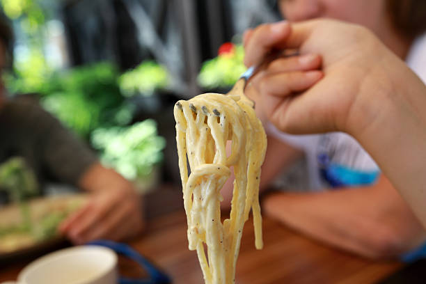 Woman twirling spaghetti with creamy sauce on a fork. Delicious italian food for dinner or lunch. Pasta meal concept.