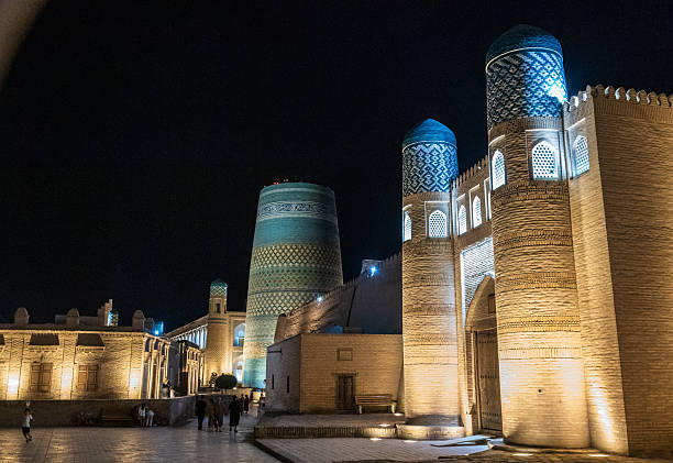 Khiva, Uzbekistan - July 31, 2025. Night time view of the historic city center of Khiva, looking out at the Kalta Minor Minaret. People are strolling along.