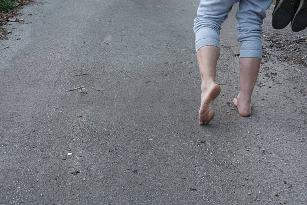 Close-up of man's feet walking barefoot on a gray asphalt road, enjoying the connection with nature