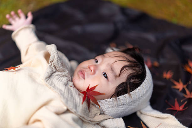 Baby boy lying down in public park, a maple leaf is on his cheek