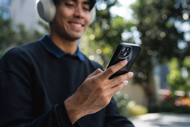 Young man relaxing by the sidewalk, scrolling through his smartphone while music plays through his headphones, enjoying a moment of quiet leisure and the beauty of the city around him
